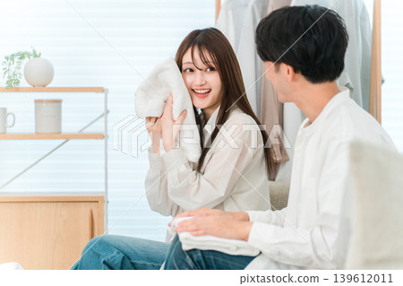 Smiling couple folding laundry in the living room (bath towels, texture, finish) 139612011