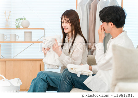 A couple folding towels in the living room, troubled by the musty smell of damp laundry. A couple folding towels in the living room, troubled by the musty smell of damp laundry. 139612013