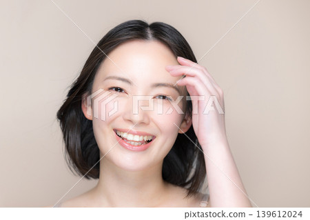 A woman with flowing black hair and a smile, against a beige background, is shown with beautiful skin and skincare, suggesting beauty and treatment ideas. A woman with flowing black hair and a smile, against a beige background, is shown with beautiful skin and skincare, suggesting beauty and treatment ideas. 139612024