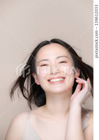 A woman with flowing black hair and a smile, against a beige background, is shown with beautiful skin and skincare, suggesting beauty and treatment ideas. A woman with flowing black hair and a smile, against a beige background, is shown with beautiful skin and skincare, suggesting beauty and treatment ideas. 139612033