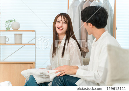 一對面帶著微笑的夫婦在客廳裡疊衣服（參與家務，分擔家務） 139612111
