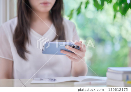 A young woman studying while looking at her smartphone. A young woman studying while looking at her smartphone. 139612175