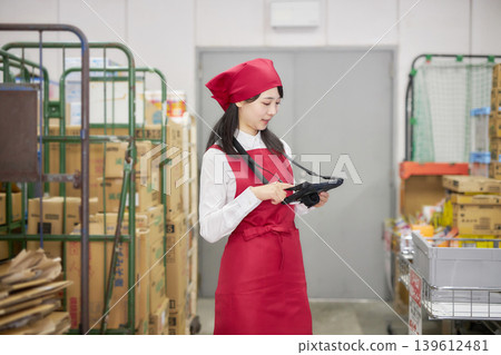 A young woman manages inventory using a tablet in the back room. A young woman manages inventory using a tablet in the back room. 139612481