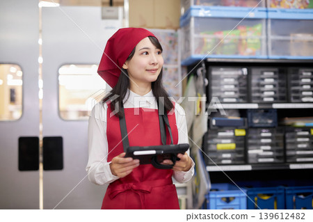 A young woman manages inventory using a tablet in the back room. A young woman manages inventory using a tablet in the back room. 139612482