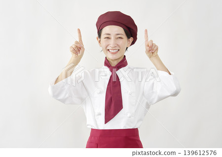 A female pastry chef points upwards. A female pastry chef points upwards. 139612576