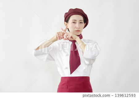 一位女糕點師面帶微笑，雙手比出「X」型手勢。 139612593