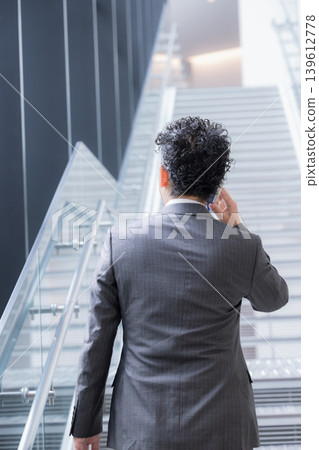 一位留著鬍子的中年男子背對著鏡頭,給人一種商人一邊在辦公室裡爬樓梯一邊打電話的印象,展現出他在銷售方面的活力和速度。 一位留著鬍子的中年男子背對著鏡頭,給人一種商人一邊在辦公室裡爬樓梯一邊打電話的印象,展現出他在銷售方面的活力和速度。 139612778