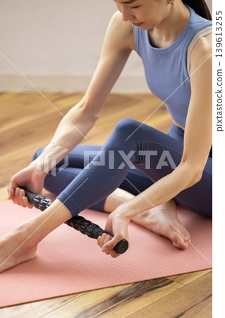 A close-up of the hands of a woman in yoga wear using a massage roller for self-massage. A close-up of the hands of a woman in yoga wear using a massage roller for self-massage. 139613255