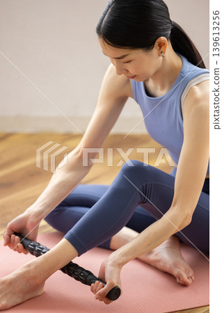 A middle-aged Japanese woman in yoga wear uses a massage roller to give herself a self-massage. 139613256