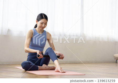 一位身穿瑜珈服的中年日本女性正在使用按摩滾筒進行自我按摩。 139613259