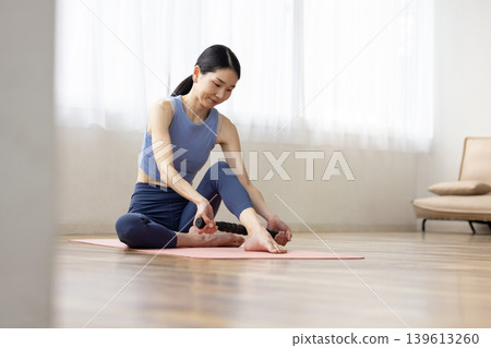 A middle-aged Japanese woman in yoga wear uses a massage roller to give herself a self-massage. A middle-aged Japanese woman in yoga wear uses a massage roller to give herself a self-massage. 139613260