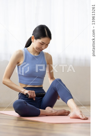 一位身穿瑜珈服的中年日本女性正在使用按摩滾筒進行自我按摩。 139613261