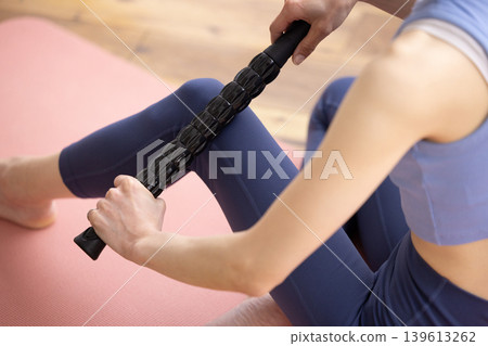 一位身穿瑜珈服的女士正在使用按摩滾輪進行自我按摩，鏡頭特寫她的雙手。 139613262