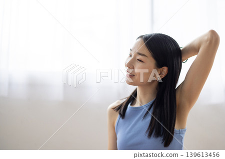 A middle-aged Japanese woman relaxes and smiles by a bright window. A middle-aged Japanese woman relaxes and smiles by a bright window. 139613456