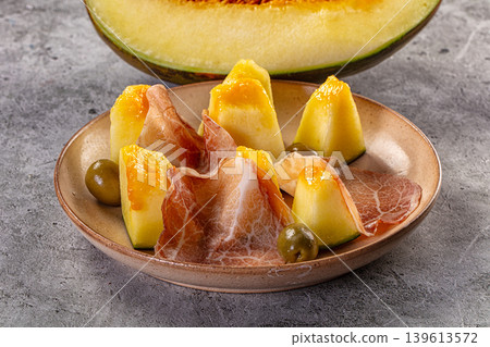 Gourmet appetizer of fresh melon with slices of prosciutto ham and olives on a rustic plate 139613572