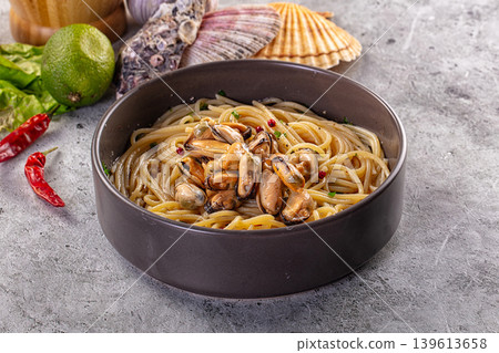 Spaghetti with mussels and pink peppercorns in a gray bowl on a rustic table 139613658
