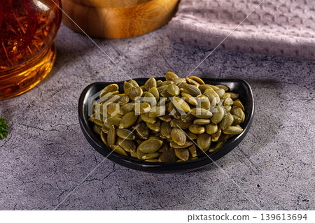 A small black bowl of healthy shelled pumpkin seeds or pepitas on a rustic grey tabletop A small black bowl of healthy shelled pumpkin seeds or pepitas on a rustic grey tabletop 139613694