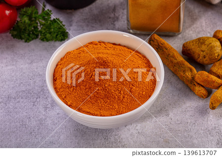 Bright turmeric powder in white bowl with fresh spices and vegetables 139613707