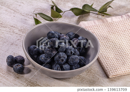 Ripe blueberries in ceramic bowl, scattered on rustic table with green leaves 139613709