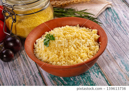 Cooked couscous in rustic clay bowl with fresh tomatoes and herbs on wooden table Cooked couscous in rustic clay bowl with fresh tomatoes and herbs on wooden table 139613736