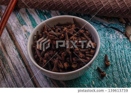 Dried cloves in white bowl with wooden spoon on rustic table Dried cloves in white bowl with wooden spoon on rustic table 139613739