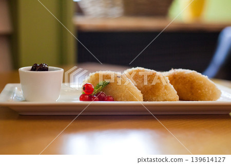 Sweet fried pastries with berry jam and redcurrant garnish on white plate 139614127
