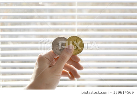 Two Bitcoin coins in a woman's hand in front of a closed window Two Bitcoin coins in a woman's hand in front of a closed window 139614569