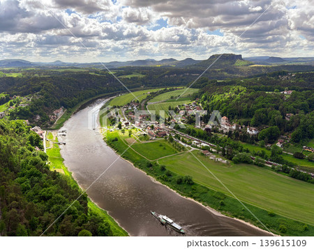 A panoramic, picturesque view of the Elbe River bend in the Saxon Switzerland National Park against a blue cloudy sky. A panoramic, picturesque view of the Elbe River bend in the Saxon Switzerland National Park against a blue cloudy sky. 139615109
