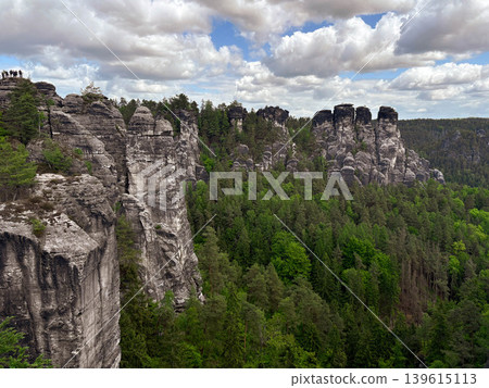a stunning natural landscape dominated by massive, weathered sandstone rock pillars rising dramatically from a dense green forest. Saxon Switzerland in Germany. a stunning natural landscape dominated by massive, weathered sandstone rock pillars rising dramatically from a dense green forest. Saxon Switzerland in Germany. 139615113