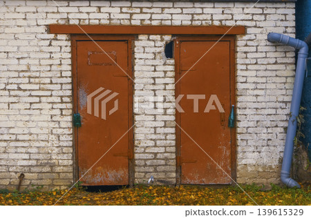 Worn metal handles and fallen foliage create nostalgic autumn vibe on weathered building facade Worn metal handles and fallen foliage create nostalgic autumn vibe on weathered building facade 139615329