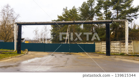 Rainy street with pipes. Quiet industrial area with reflective wet asphalt and blue fencing Rainy street with pipes. Quiet industrial area with reflective wet asphalt and blue fencing 139615344