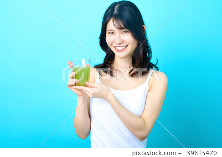 A young Japanese woman smiles while holding a glass of green juice. 139615470