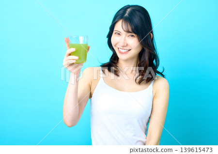 一位年輕的日本女子麵帶微笑,舉起一杯綠色果汁。乾杯! 一位年輕的日本女子麵帶微笑,舉起一杯綠色果汁。乾杯! 139615473