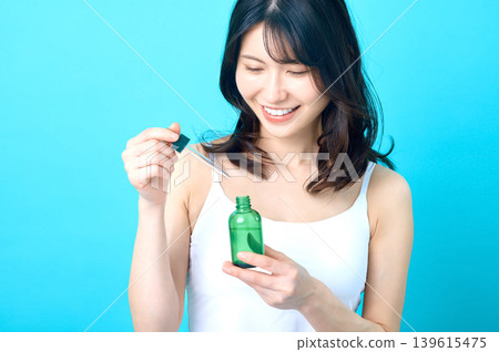 A young Japanese woman smiles as she looks at a beauty serum. A young Japanese woman smiles as she looks at a beauty serum. 139615475