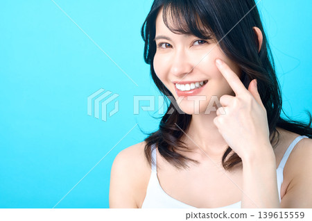 一位年輕的日本女性指著自己的臉頰,臉上帶著燦爛的笑容,表示對自己的護膚程序非常滿意。 一位年輕的日本女性指著自己的臉頰,臉上帶著燦爛的笑容,表示對自己的護膚程序非常滿意。 139615559