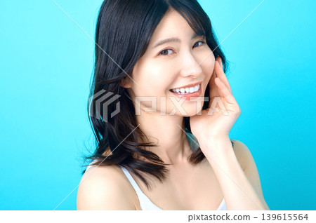 一位年輕的日本女子麵帶微笑,一手輕撫臉頰,展現出美麗的肌膚。 一位年輕的日本女子麵帶微笑,一手輕撫臉頰,展現出美麗的肌膚。 139615564