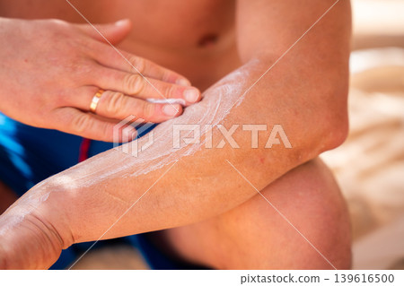 Caucasian man applying sunscreen cream on arm while sitting on a beach during a summer vacation at a seaside resort. Sun protection and skincare routine Caucasian man applying sunscreen cream on arm while sitting on a beach during a summer vacation at a seaside resort. Sun protection and skincare routine 139616500