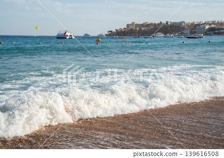 Sea waves on a sandy beach in Sharm El Sheikh on the Red Sea coast with boats and resort buildings in Egypt. Summer travel and seaside tourism Sea waves on a sandy beach in Sharm El Sheikh on the Red Sea coast with boats and resort buildings in Egypt. Summer travel and seaside tourism 139616508