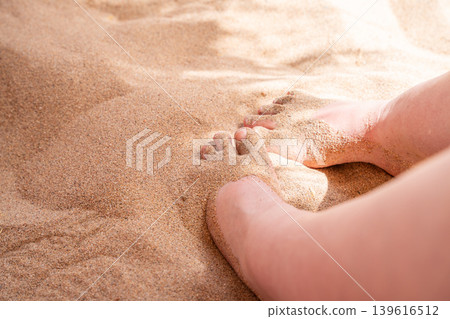 Bare feet covered with warm beach sand during summer vacation on seaside coast under bright sunlight. Relaxation and wellness lifestyle Bare feet covered with warm beach sand during summer vacation on seaside coast under bright sunlight. Relaxation and wellness lifestyle 139616512