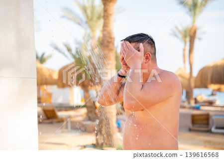 Caucasian man washing face under an outdoor beach shower at a Red Sea resort in Sharm El Sheikh Egypt. Summer hygiene and resort lifestyle 139616568
