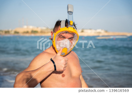 Caucasian man in a full face snorkeling mask showing thumbs up on the Red Sea beach in Sharm El Sheikh Egypt. Summer diving and resort lifestyle Caucasian man in a full face snorkeling mask showing thumbs up on the Red Sea beach in Sharm El Sheikh Egypt. Summer diving and resort lifestyle 139616569