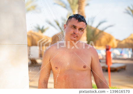 Caucasian man standing under an outdoor beach shower at a Red Sea resort in Sharm El Sheikh Egypt. Summer hygiene and resort lifestyle Caucasian man standing under an outdoor beach shower at a Red Sea resort in Sharm El Sheikh Egypt. Summer hygiene and resort lifestyle 139616570
