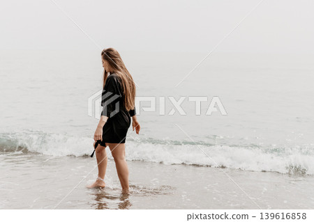 Woman beach ocean walking along the shoreline in a black robe on a foggy day with copy space for travel Woman beach ocean walking along the shoreline in a black robe on a foggy day with copy space for travel 139616858