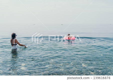 Swimming ocean vacation woman in white swimsuit and sunglasses enjoys a sunny day at the sea with a person on a pink inflatable ring Swimming ocean vacation woman in white swimsuit and sunglasses enjoys a sunny day at the sea with a person on a pink inflatable ring 139616878