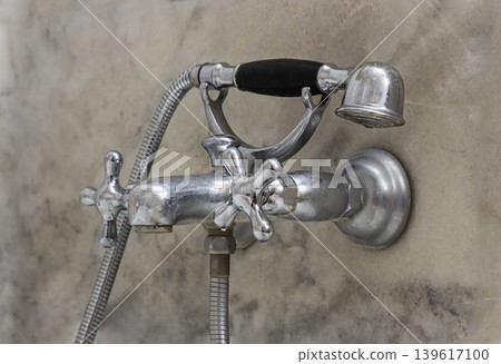 This exquisite vintage bath fixture, balances old-world charm with functional luxury. A telephone-style hand shower with a black grip rests on a chrome cradle above two sculpted cross-handle taps. The This exquisite vintage bath fixture, balances old-world charm with functional luxury. A telephone-style hand shower with a black grip rests on a chrome cradle above two sculpted cross-handle taps. The 139617100