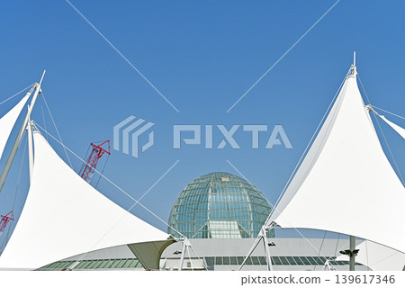 A white tent overlooking a glass dome; the modern architectural beauty of the aquarium stands out against the blue sky. 139617346
