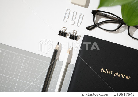 Flat lay of black planner with paper clips, binder clips, glasses, eraser, and cutting mat on white background. Copyspace Flat lay of black planner with paper clips, binder clips, glasses, eraser, and cutting mat on white background. Copyspace 139617645