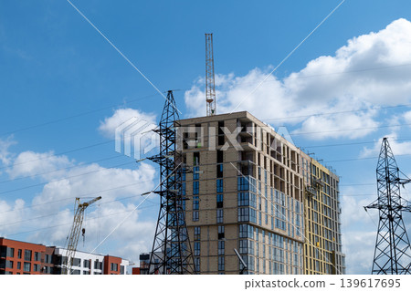 Workers are constructing a multi storey building with cranes and power lines present at the site on a clear day with clouds Workers are constructing a multi storey building with cranes and power lines present at the site on a clear day with clouds 139617695
