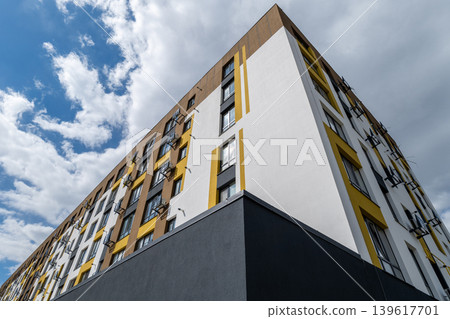 A modern apartment building stands tall with its unique design in an urban location on a cloudy day with blue and white skies A modern apartment building stands tall with its unique design in an urban location on a cloudy day with blue and white skies 139617701