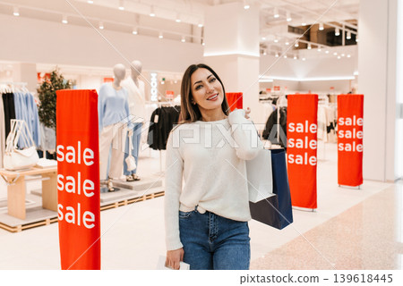 Happy Female Shopper Pauses near Sale Display with Purchased Items Happy Female Shopper Pauses near Sale Display with Purchased Items 139618445